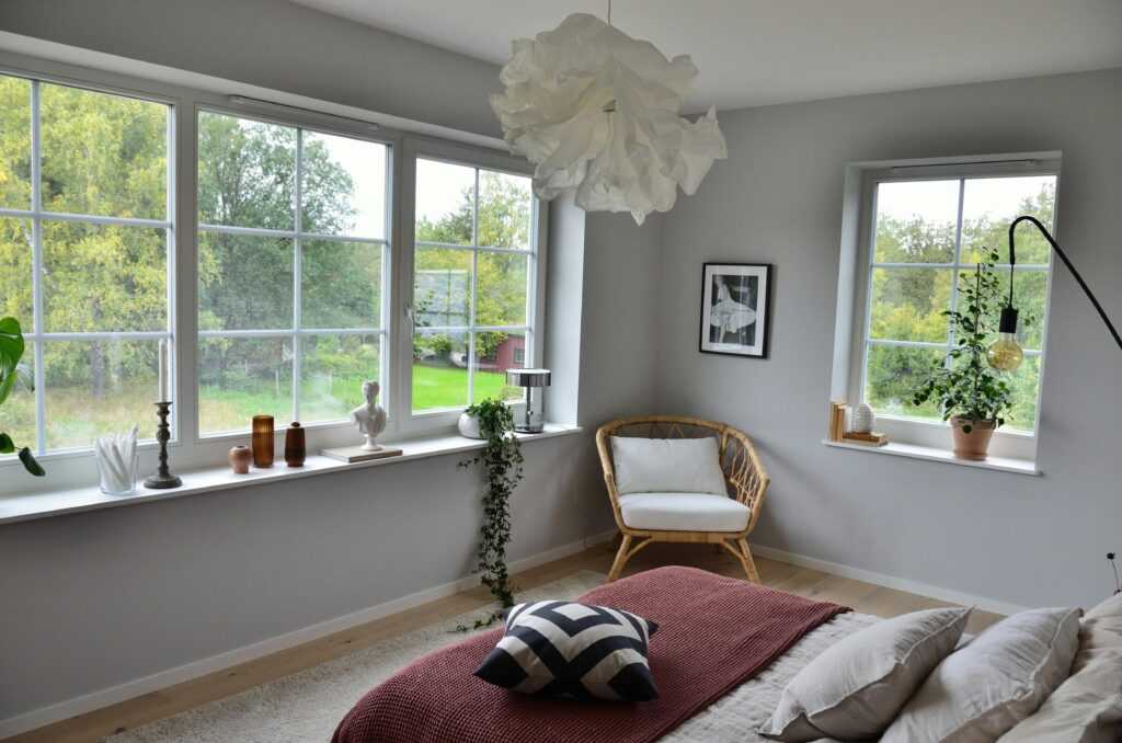 Cozy Scandinavian bedroom with natural light and modern decor, featuring large windows and greenery.